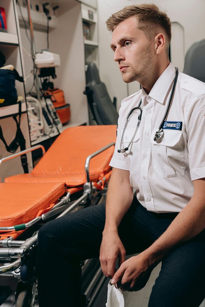 A paramedic in uniform sitting inside an ambulance next to a gurney, ready for an emergency.