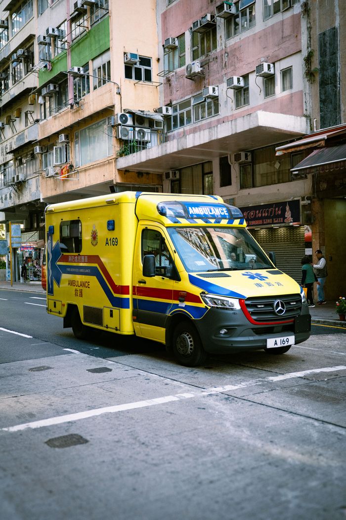 Yellow ambulance on an urban street in front of colorful residential buildings.
